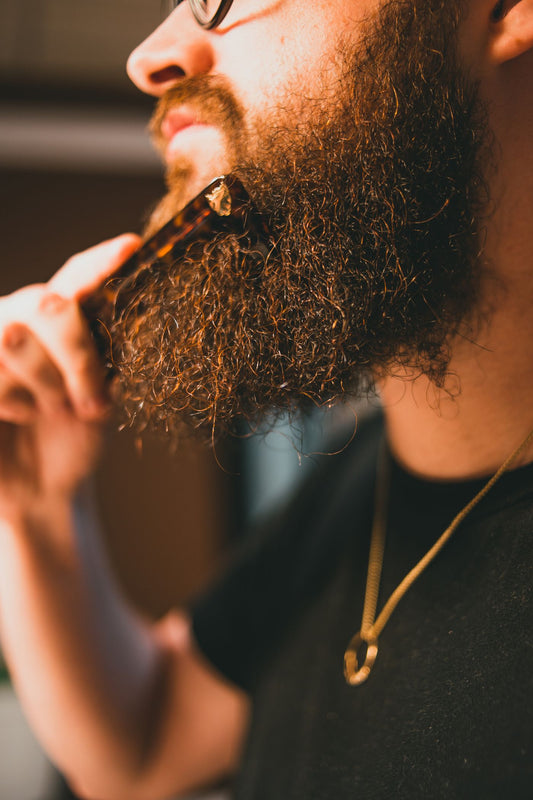 Close-up of a man combing his beard with a tortoiseshell comb.