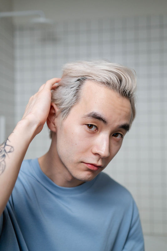Man shaping his short blonde hair with his hand in a bathroom.