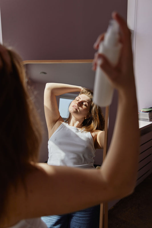 Woman lifting her hair while holding a spray bottle in front of a mirror