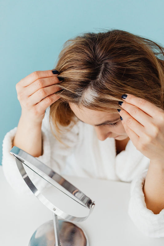 Woman parting her hair to check visible grey regrowth in a mirror