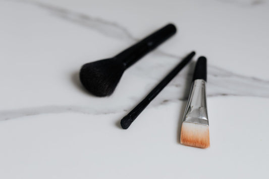 Three makeup brushes on a pale marble surface, with makeup residue visible on the flat brush.
