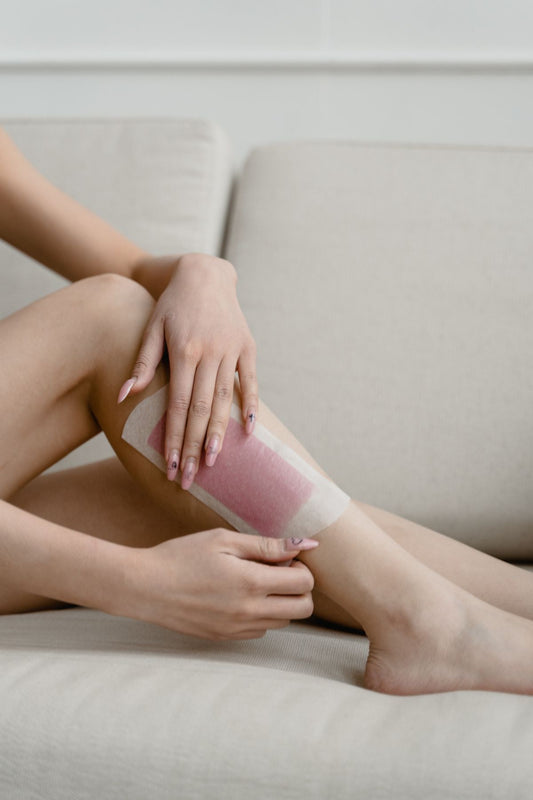 Close-up of a woman pressing a pink wax strip onto her lower leg