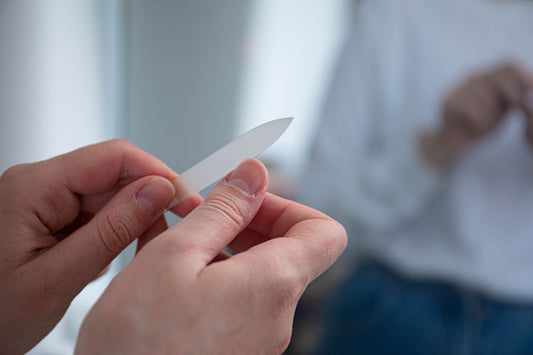 Close-up of a person using a glass nail file along the edge of a natural thumbnail