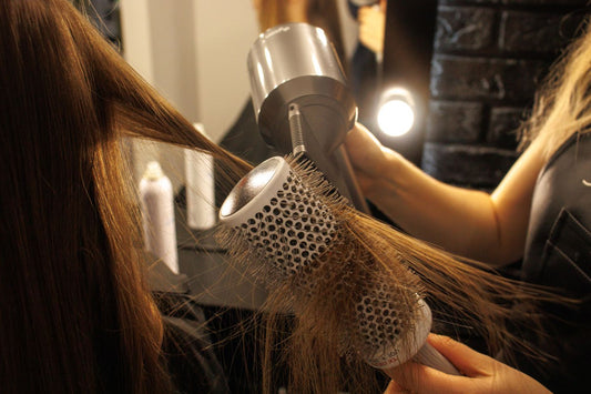 Hairdresser using a round brush and hairdryer to shape a section of long brown hair